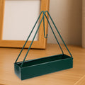 Triangular iron mosquito coil holder in a lush garden setting.