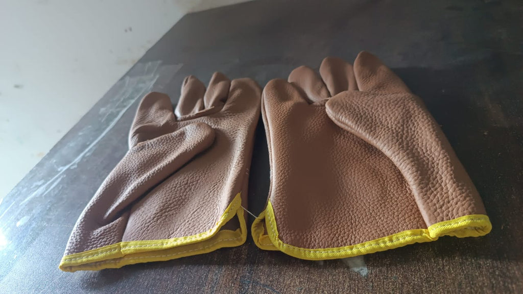 Close-up of a gardener's hand wearing a BraveVault leather glove, holding a small garden tool.