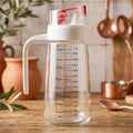 Glass oil dispenser bottle with auto-flip cap, side handle, and measurement scale for precise kitchen pouring